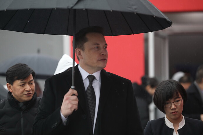 Elon Musk mit einem schwarzen Regenschirm