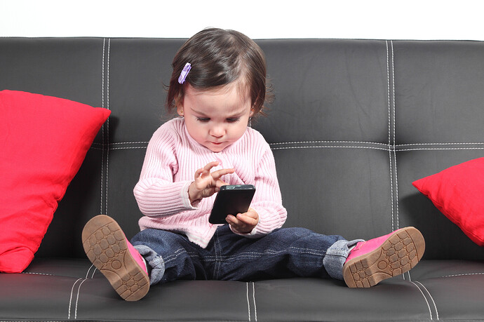 Ein Baby, das zu Hause auf dem Sofa sitzt und mit einem Smartphone spielt