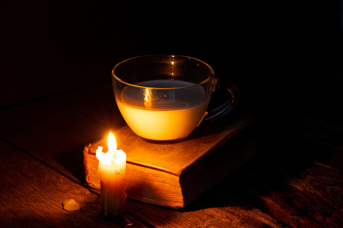 Auf einem Holztisch eine Kerze, eine Tasse Milch und ein Buch.