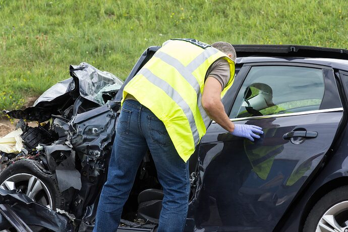 Mann mit Sicherheitsweste schaut in einen durch Kollision stark beschädigten Ford