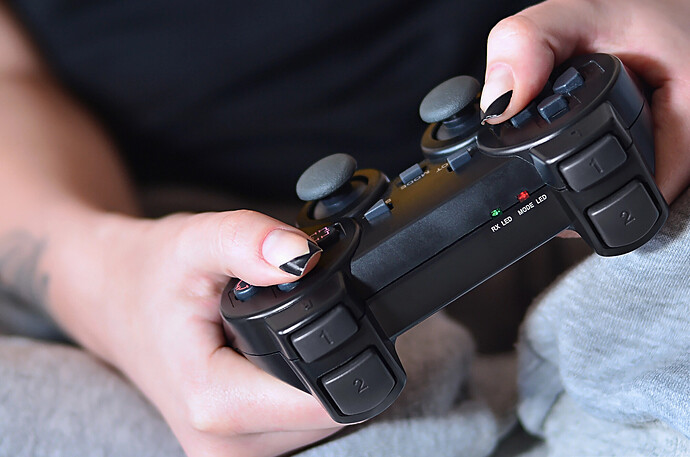 Ein Mädchen in grauer Hose hält einen schwarzen, Game-Controller