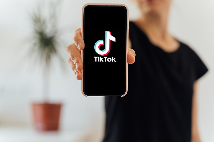 TikTok-App auf dem Display eines Mobiltelefons in der Hand einer Frau