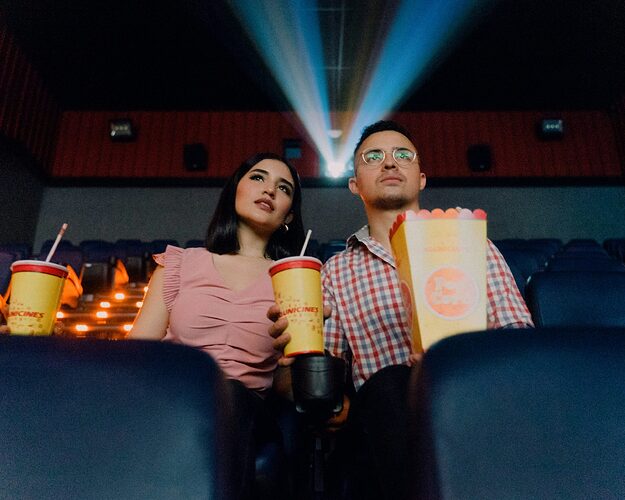 Ein Paar sitzt im Kino mit Popcorn und Getränk.