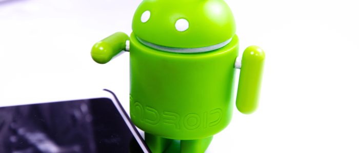 Grüne Android-Figur auf weißem Hintergrund mit Smartphone