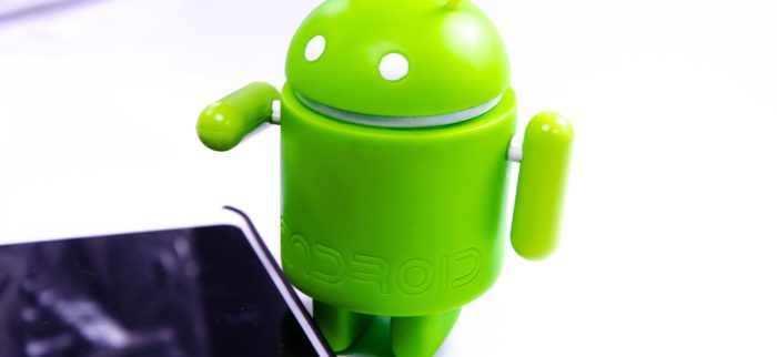 Grüne Android-Figur auf weißem Hintergrund mit Smartphone