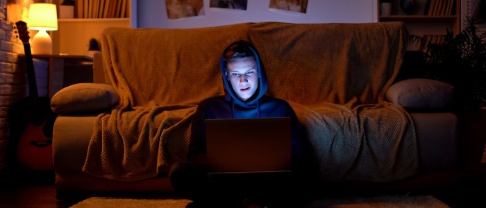 Junger Hacker mit Kapuzenpulli, der mit seinem Laptop in Websites eindringt