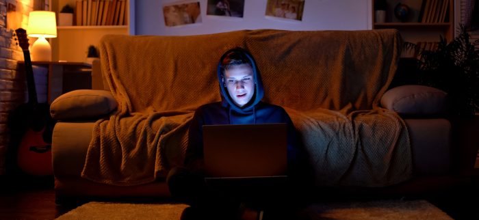 Junger Hacker mit Kapuzenpulli, der mit seinem Laptop in Websites eindringt