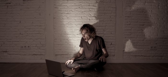 Ein junger Mann sitzt verängstigt vor seinem Laptop