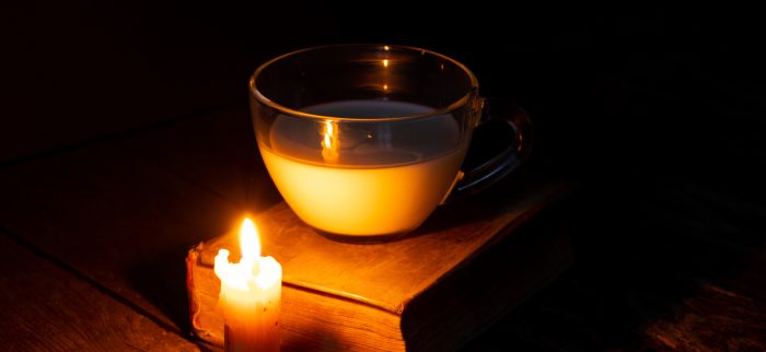 Auf einem Holztisch eine Kerze, eine Tasse Milch und ein Buch.