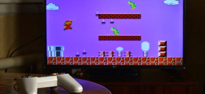 Videospiel-Controller auf einem Tisch mit dem Spiel Super Mario Bros auf einem Bildschirm im Hintergrund