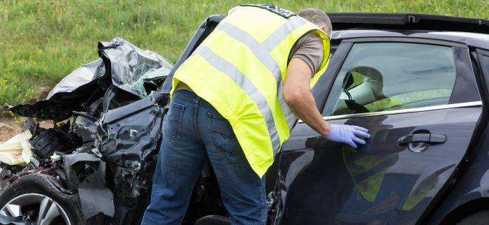 Mann mit Sicherheitsweste schaut in einen durch Kollision stark beschädigten Ford