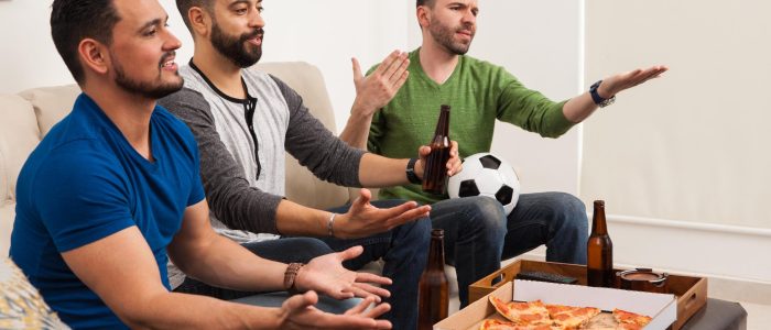 Drei Fußballfreunde schauen sich ein Spiel an und essen Pizza