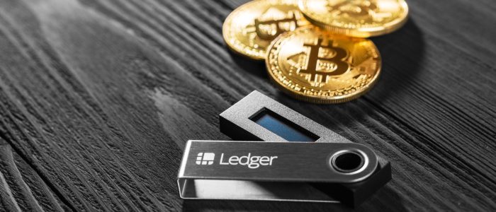 Eine Hardware-Wallet von Ledger und drei physische Bitcoins auf einem dunklen Untergrund