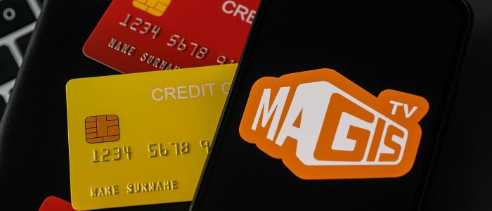 Auf einem Laptop liegen ein Smartphone mit MagisTV-Logo und rote sowie gelbe Kreditkarten. Das Bild symbolisiert die Gefahr des Datenklaus durch Malware in Streaming-Apps.