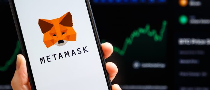 Smartphone mit MetaMask-Logo und Krypto-Kursverlauf im Hintergrund