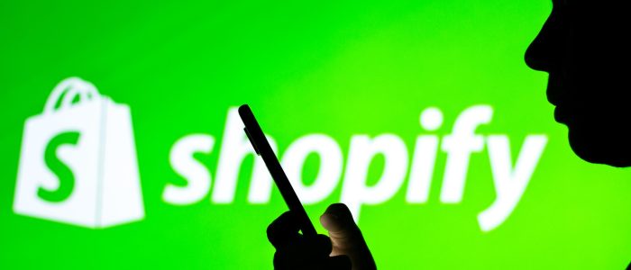 Schatten einer Person, die auf ihr Smartphone schaut mit Shopify-Logo im Hintergrund