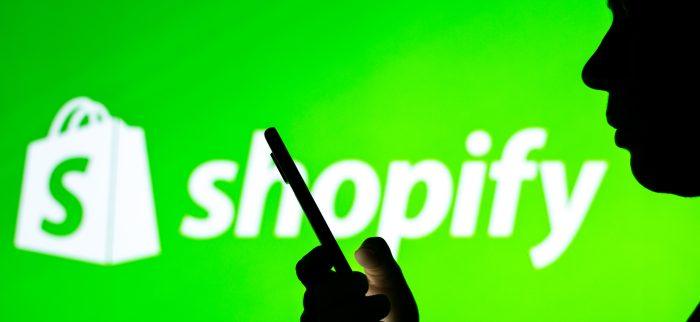 Schatten einer Person, die auf ihr Smartphone schaut mit Shopify-Logo im Hintergrund
