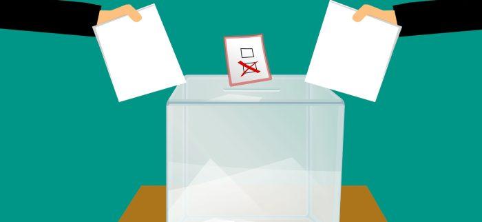 Zwei Hände werfen Stimmzettel in eine Wahlurne
