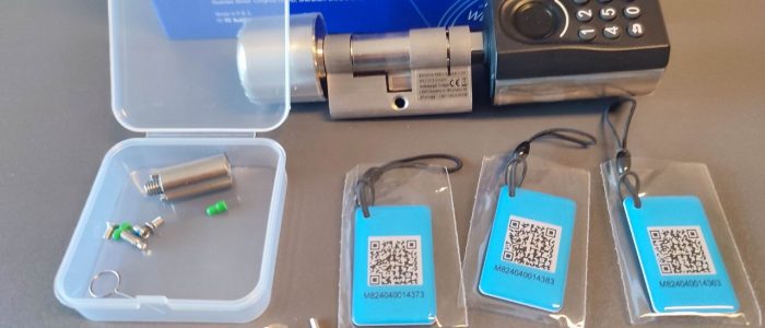 Nahaufnahme des vollständigen Lieferumfangs des WELOCK Touch A51 Smart Locks: Auf dem Bild sind das Türschloss mit Tastenfeld, eine geöffnete Kunststoffbox mit Montagematerial, drei RFID-Karten, ein Innensechskantschlüssel und ein kleiner Schraubendreher vor der Produktverpackung zu sehen.