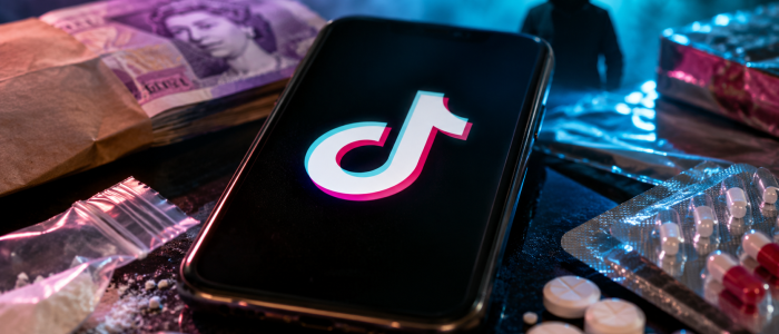 Smartphone mit TikTok-Logo neben Falschgeld, Drogen und verschreibungspflichtigen Medikamenten