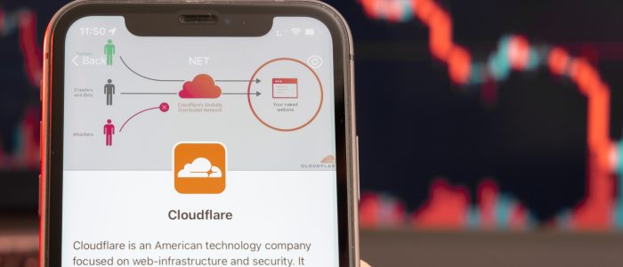 Smartphone mit einer Cloudflare-Anwendung und einem fallenden Aktienkurs im Hintergrund