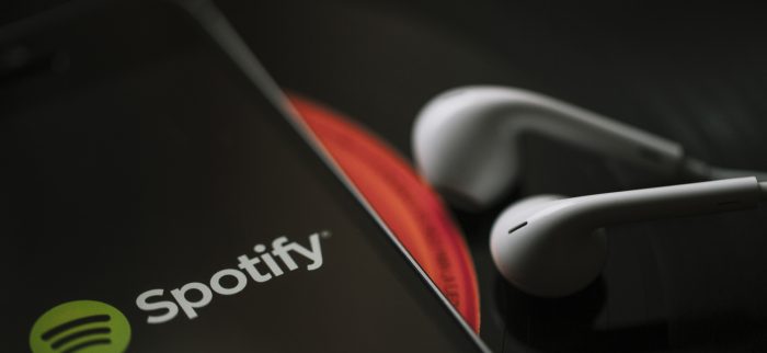 Handy mit dem Spotify auf dem Display und weißen Kopfhörern auf einer schwarzen Schallplatte