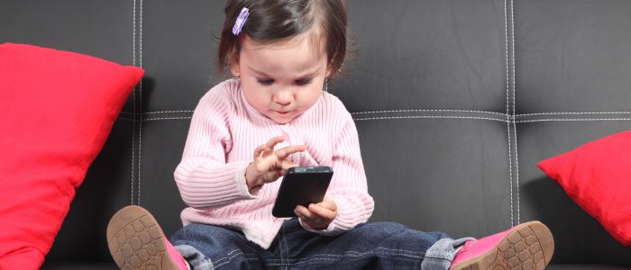 Ein Baby, das zu Hause auf dem Sofa sitzt und mit einem Smartphone spielt