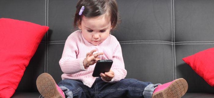 Ein Baby, das zu Hause auf dem Sofa sitzt und mit einem Smartphone spielt