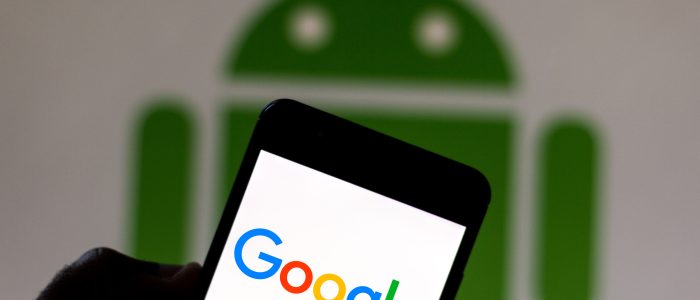 Das Google-Logo wird auf einem Smartphone angezeigt. Im Hintergrund ist das Android-Logo zu sehen