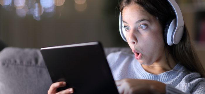 Verwundert dreinschauende Frau mit Kopfhörern prüft den Inhalt eines Tablets
