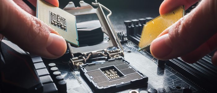 Eine Hand hält zwei CPUs vor ein Mainboard