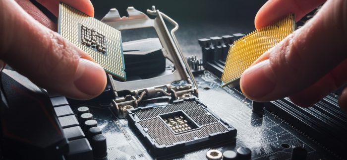 Eine Hand hält zwei CPUs vor ein Mainboard