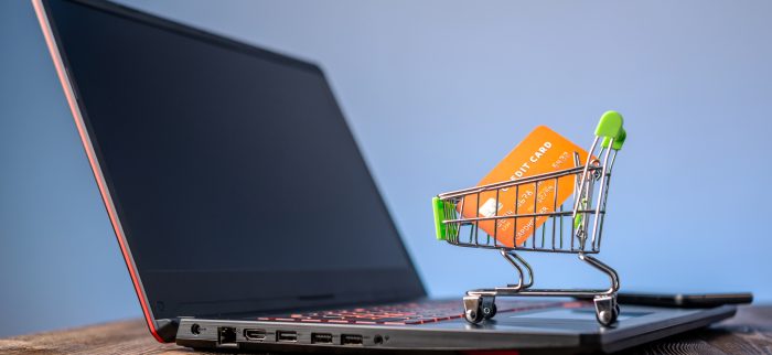 Ein Einkaufswagen mit einer Kreditkarte steht auf einem Laptop vor einem Bildschirm mit blauem Hintergrund