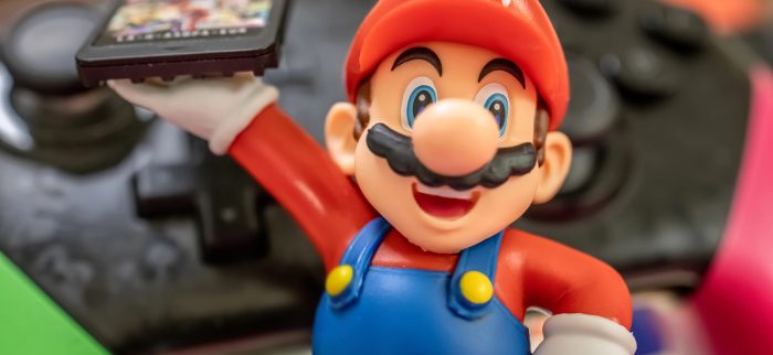 Super Mario vor einem Controller mit einem Switch-Spiel in der Hand