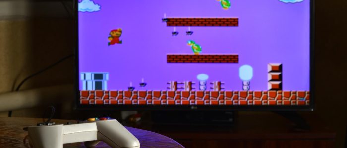 Videospiel-Controller auf einem Tisch mit dem Spiel Super Mario Bros auf einem Bildschirm im Hintergrund