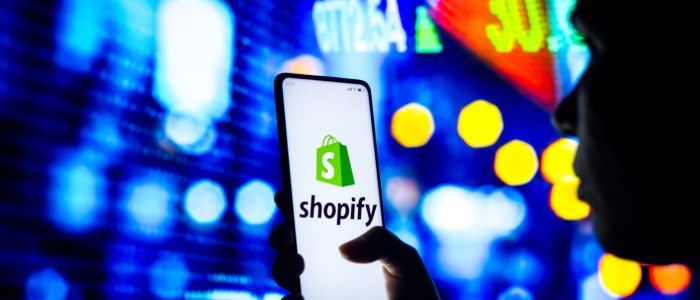 Die Silhouette einer Frau hält ein Smartphone mit dem Shopify-Logo in der Hand