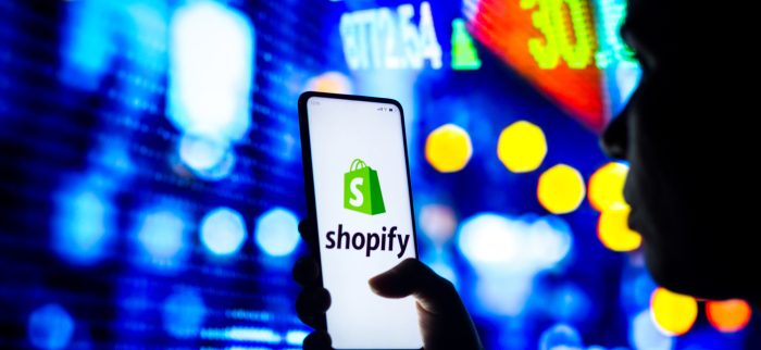 Die Silhouette einer Frau hält ein Smartphone mit dem Shopify-Logo in der Hand