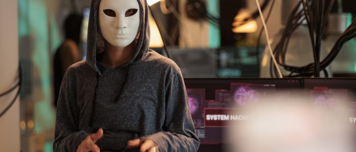 Maskierter Hacker vor Computerbildschirmen