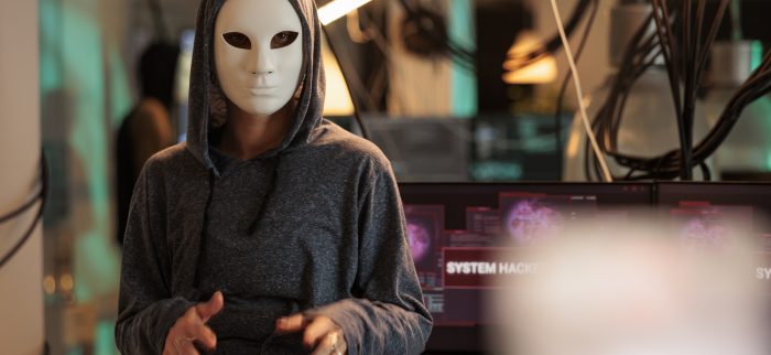 Maskierter Hacker vor Computerbildschirmen