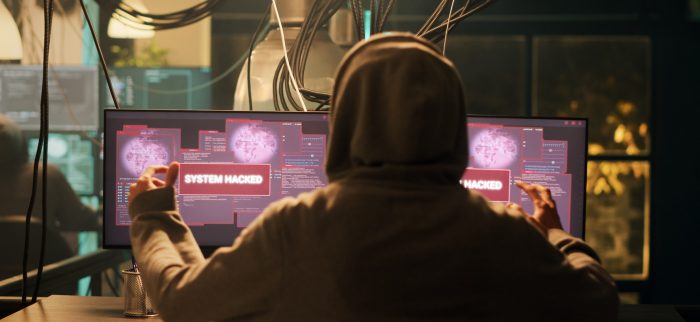 Ein junger Hacker sitzt vor seinen beiden Monitoren