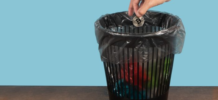 Eine Hand wirft einen Bitcoin in den Mülleimer