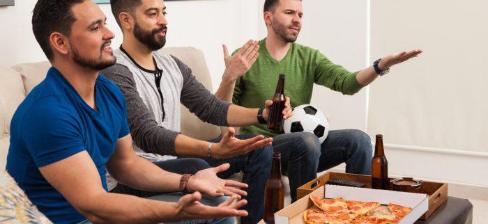 Drei Fußballfreunde schauen sich ein Spiel an und essen Pizza