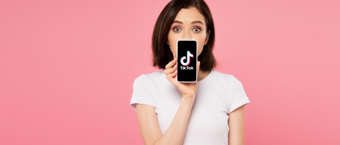 Mädchen mit überraschtem Blick hält sich ein Smartphone mit TikTok-Logo vor den Mund