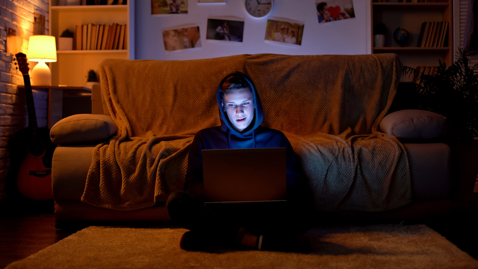 Junger Hacker mit Kapuzenpulli, der mit seinem Laptop in Websites eindringt
