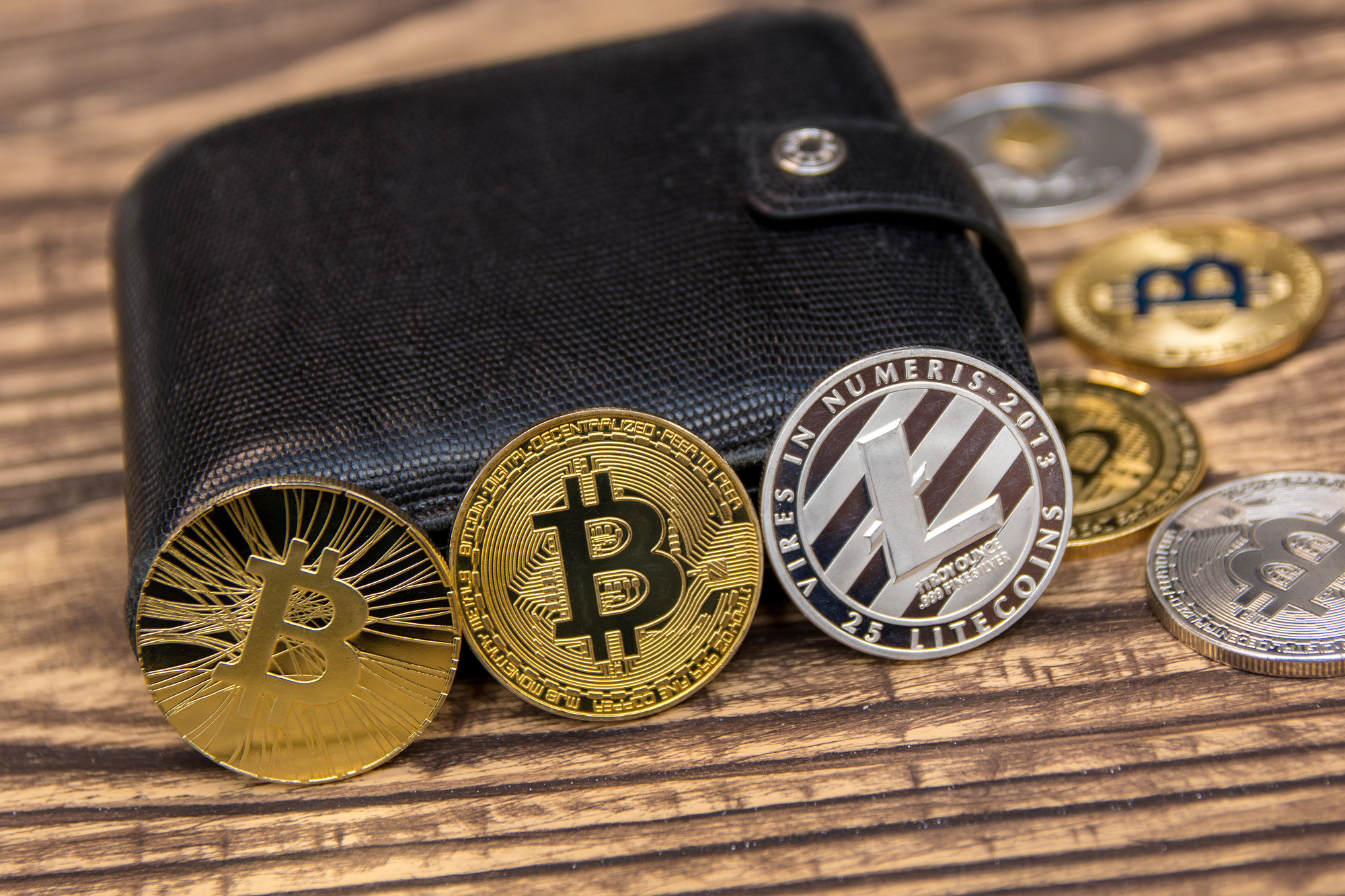Bitcoins, Litecoins und Ethereum im schwarzen Lederportemonnaie.