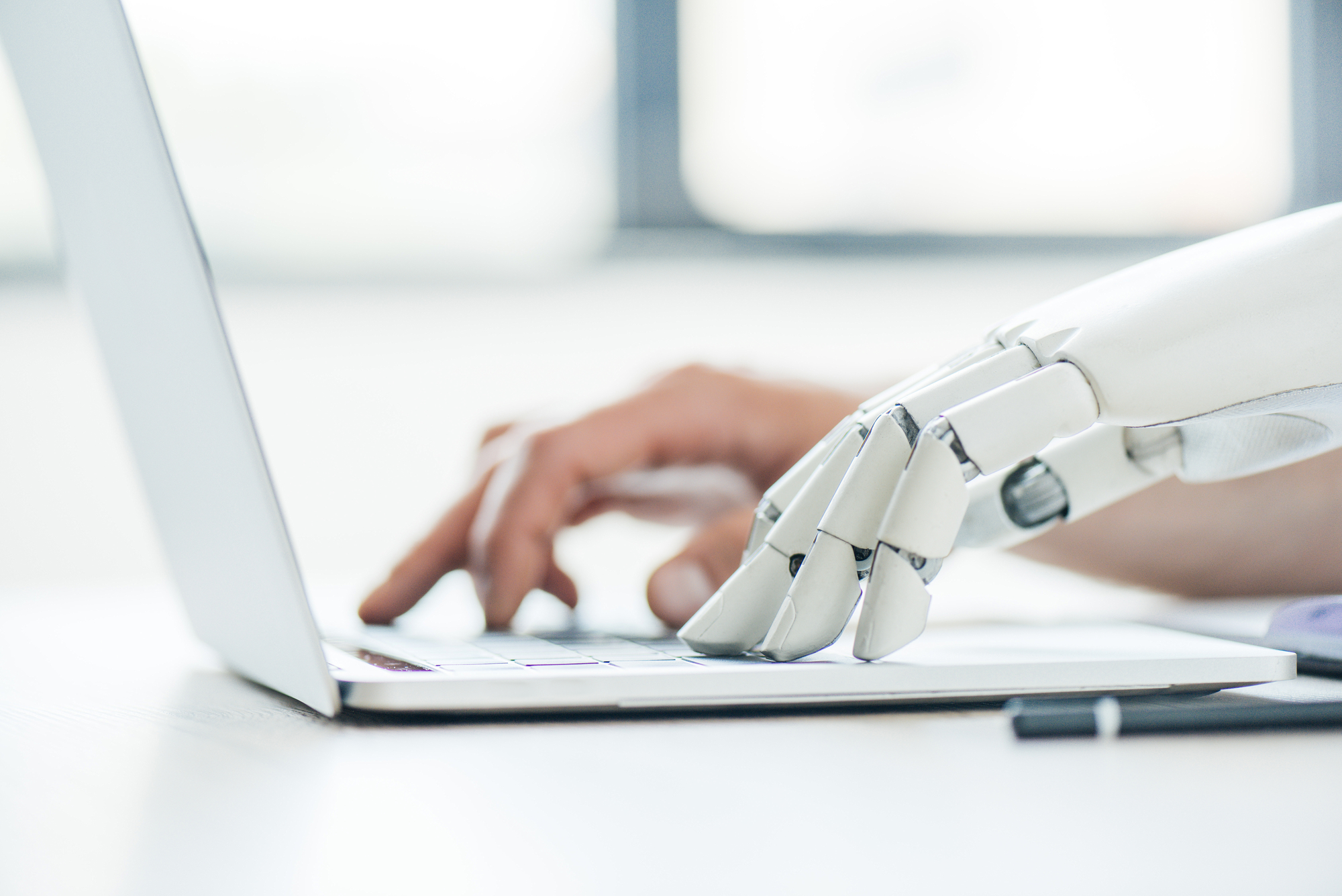 Eine menschliche Hand neben der eines Roboters auf einem Notebook