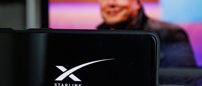 Ein Smartphone mit Starlink-Logo und Elon Musk im Hintergrund