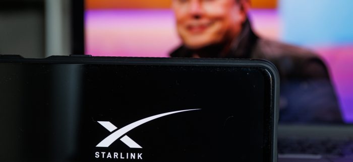 Ein Smartphone mit Starlink-Logo und Elon Musk im Hintergrund